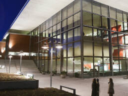 Universitetsbyggnad med stora glaspartier som lyser upp området en mörk kväll.