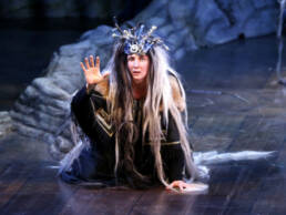 En kvinna som spelar teater på en scen omgiven av kulisser som föreställer stenar.